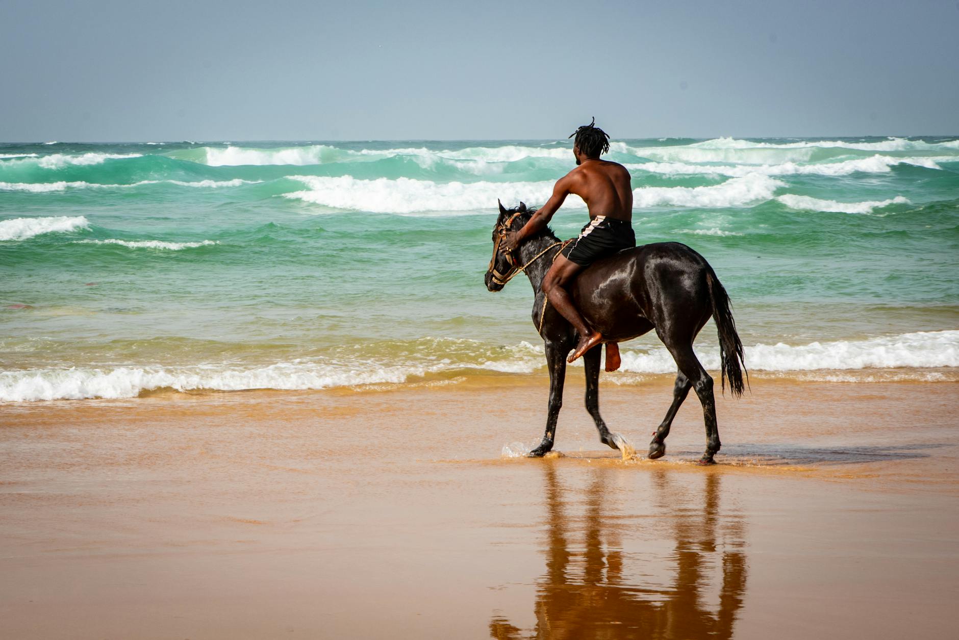 shirtless man riding a horse at the beach