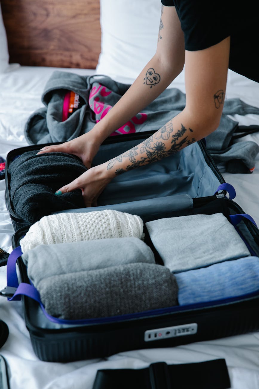 person with tattoo fixing clothes on luggage