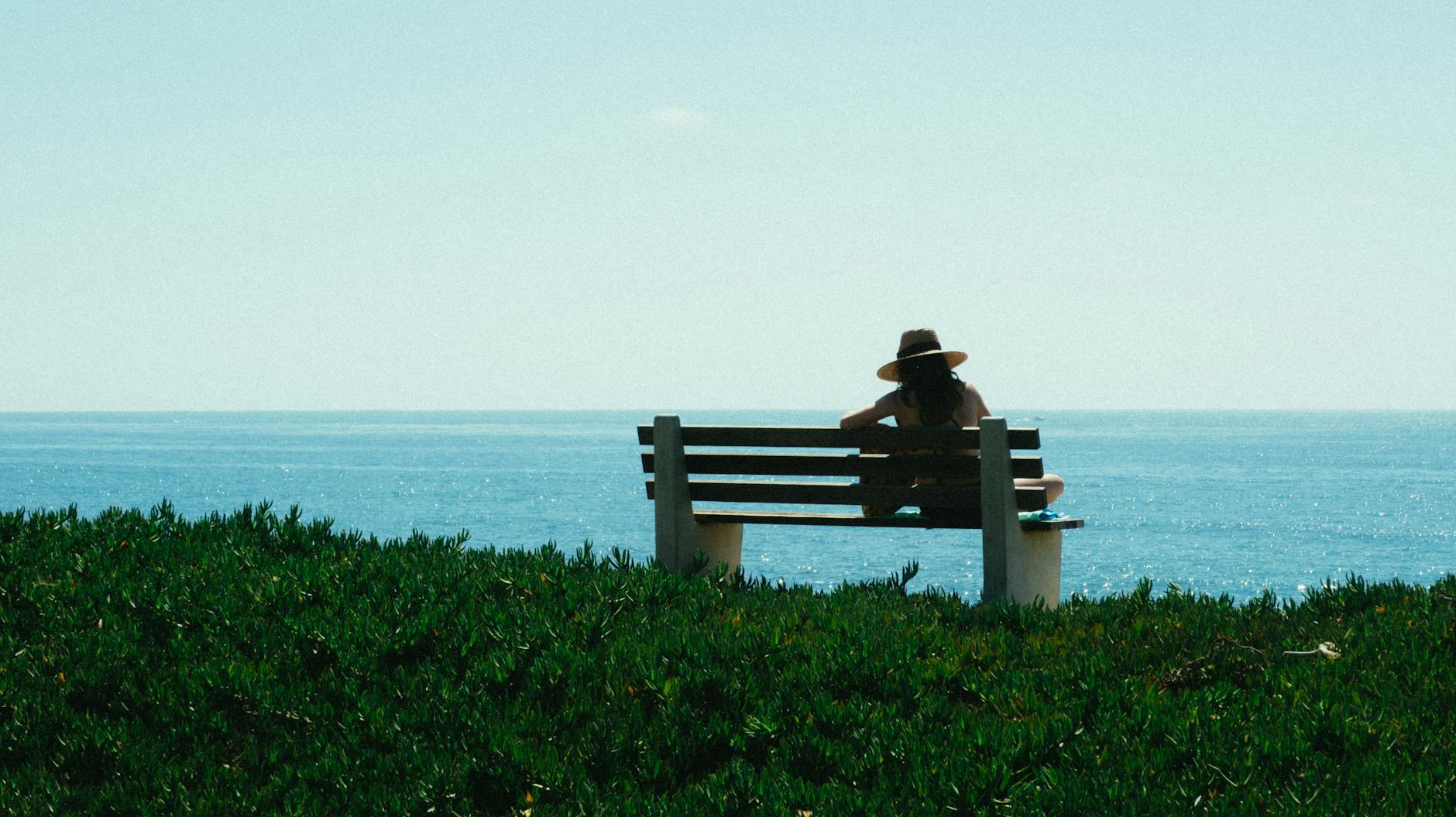 woman sitting on bench on grass shore during day